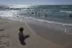A Palestinian child sits on the beach as people cool off in the Mediterranean near a tent camp by the seaside in Khan Younis, southern Gaza Strip, September 1, 2025