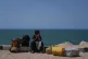 A displaced Palestinian youth sits on the curb after fleeing northern Gaza Strip, carrying his belongings along the coastal road near Wadi Gaza, September 22, 2025