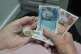 An old-age pensioner holding bank notes and coins at home in Essex