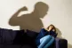 A shadow of a man with a clenched fist as a woman cowers in 