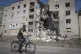 A man rides a bicycle past a building damaged in Russian she