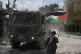 A man waves a Palestinian flag as an Israeli armored vehicle