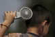 A boy cools himself with an electric fan on a sweltering day