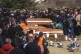 Coffins are placed next to the graves as people gather at a 