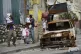 Residents walk past a burnt car as they evacuate the Delmas 