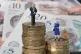 Models of a man and woman stand on a pile of coins and bank 