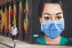 A man looks at a mural showing a nurse wearing personal prot