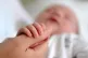 A new born baby grasping the thumb of her mother