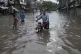 Motorcyclists drive through a flooded road caused by heavy m