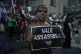 An activist covered in mud poses with a sign that reads “V